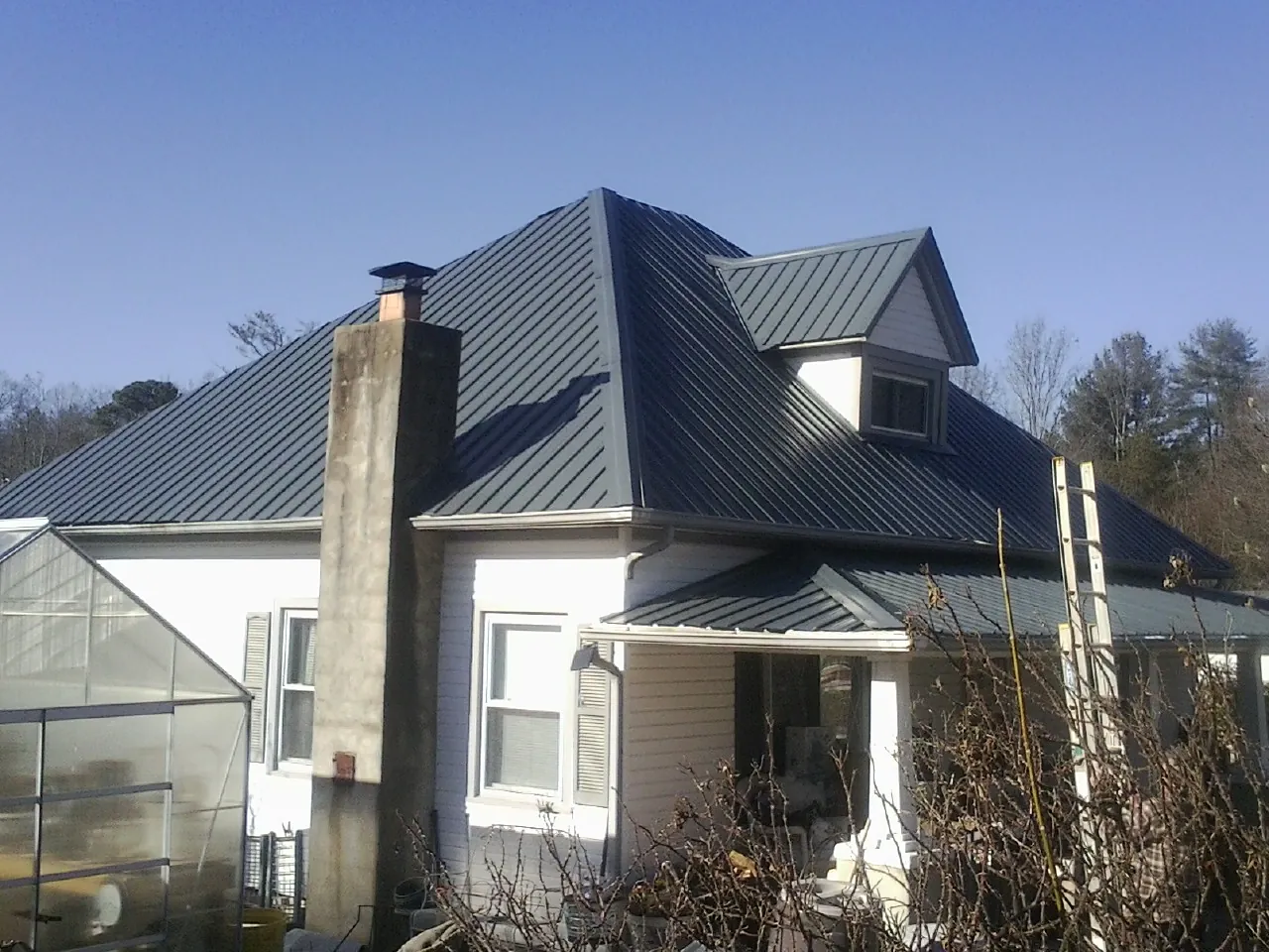 Dark blue standing seam metal roof on a white farmhouse with dormer — Slate & Tile Roof Repair by Roofing Brothers in Round Top