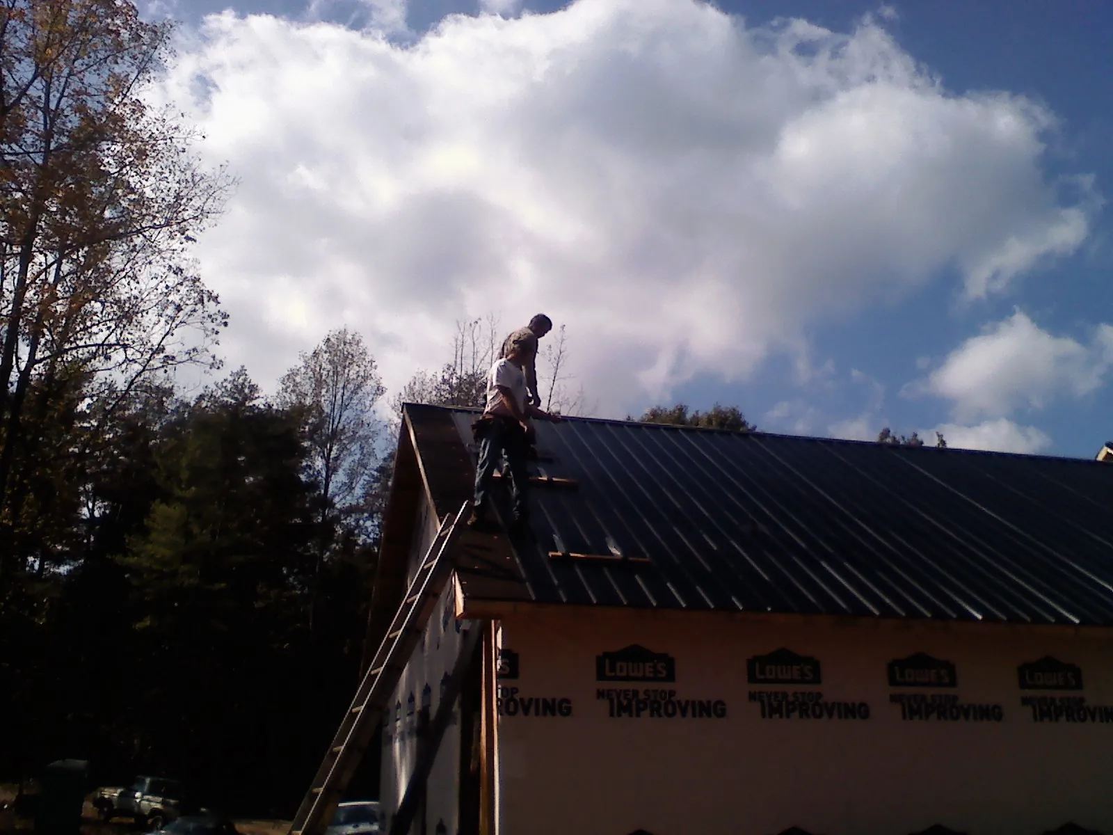 Roofer fastening dark metal panels high against a cloudy sky, from a Roof Inspection job in Round Top