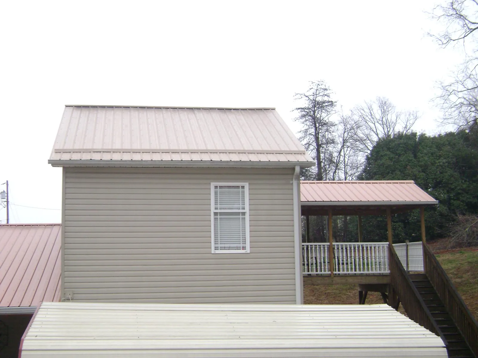Tan metal roofs on a two story addition and attached porch, from a Roof Replacement job in Round Top